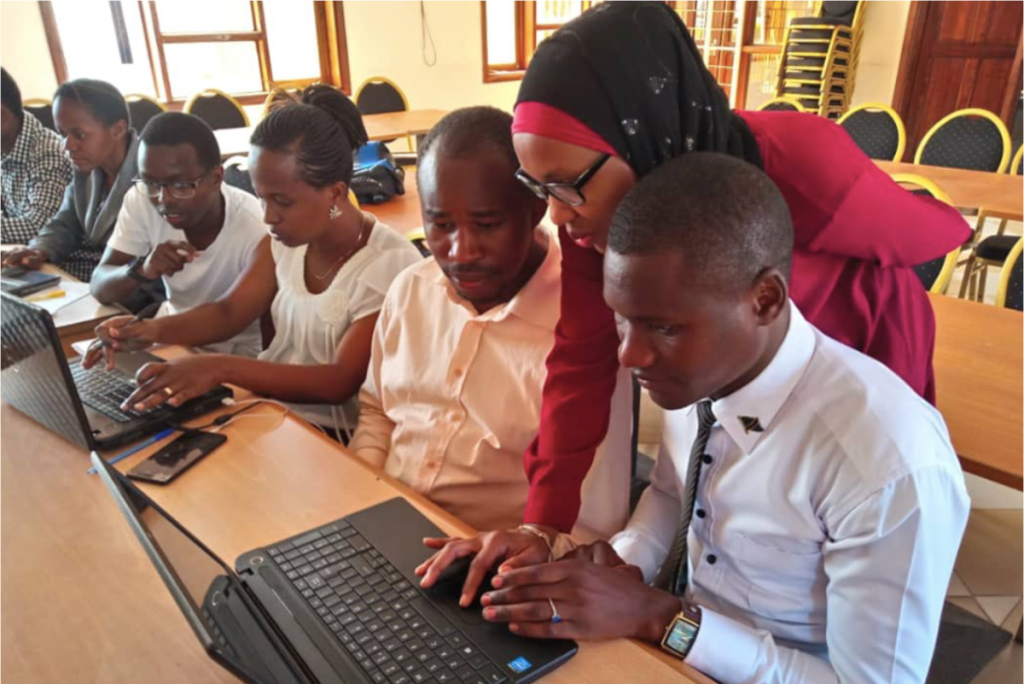 A group of students sitting with laptops while a trainer leans over them to help.