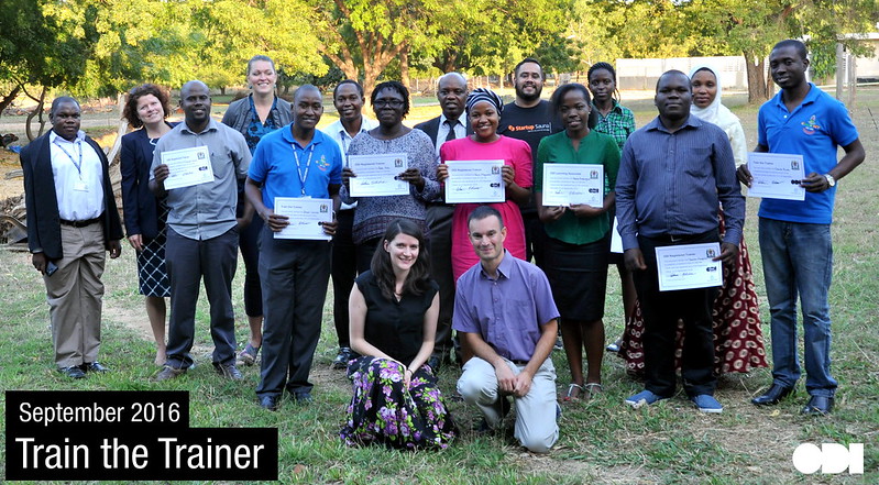 Emilie Forrest and colleague kneeling in front of a group of people holding certificates.